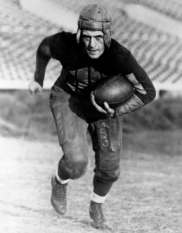 Harold "Red" Grange leans over holding the ball